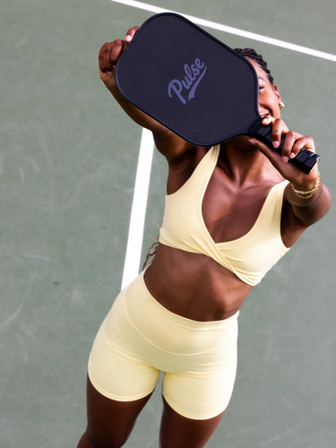 Person_holding_a_pickleball_paddle_with_Pulse_branding_on_a_tennis_court - Pulse Pickleball