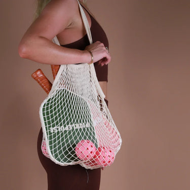 Person holding a mesh bag with pickleballs against a brown background