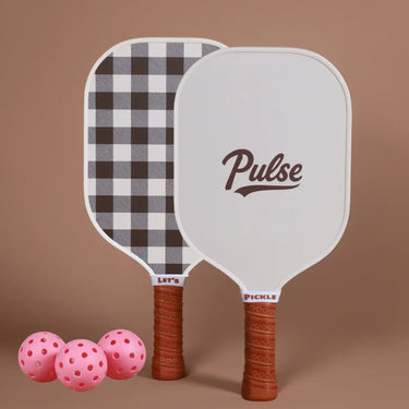 Two_pickleball_paddles_with_Pulse_branding_and_checkered_pattern_accompanied_by_pink_pickleballs_on_a_brown_background. - Pulse Pickleball