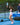 Woman playing pickleball on a blue outdoor court holding a Pulse Pickleball paddle with geometric design, smiling and enjoying a social game with Pulse branding visible in the background.”